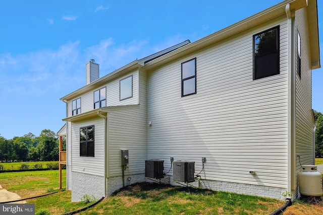 rear view of property featuring central air condition unit, a lawn, and a chimney