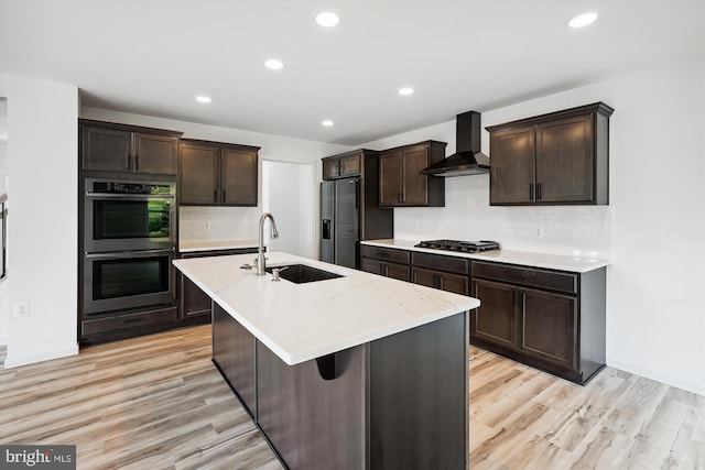 kitchen featuring a sink, stainless steel appliances, dark brown cabinets, wall chimney range hood, and light wood-type flooring