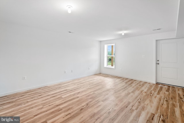 empty room with light wood finished floors, visible vents, and baseboards