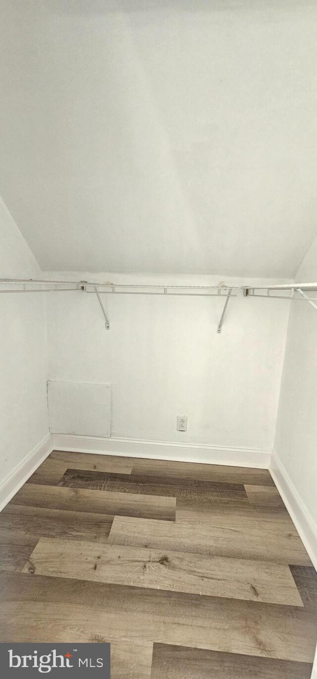 walk in closet with dark wood finished floors and vaulted ceiling