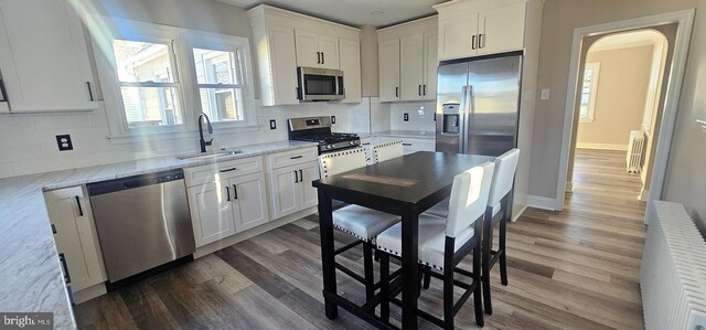 kitchen featuring appliances with stainless steel finishes, wood finished floors, arched walkways, white cabinetry, and a sink