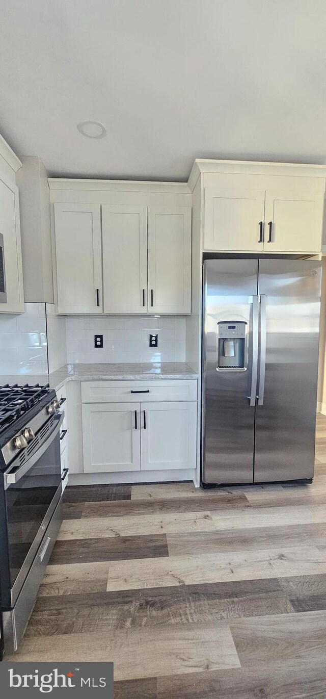 kitchen featuring light wood-type flooring, appliances with stainless steel finishes, decorative backsplash, and light countertops