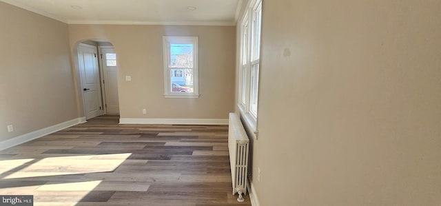 unfurnished room with crown molding, radiator, baseboards, and arched walkways