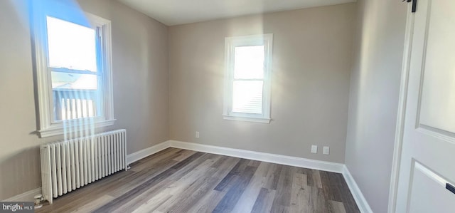 empty room featuring baseboards, radiator, and wood finished floors