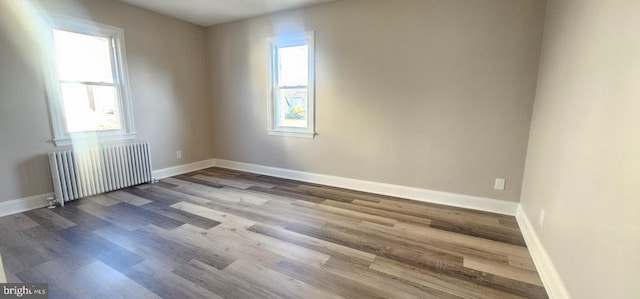 unfurnished room featuring radiator heating unit, wood finished floors, plenty of natural light, and baseboards