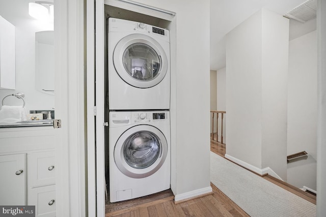 washroom with visible vents, wood finished floors, stacked washing maching and dryer, baseboards, and laundry area