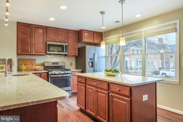 kitchen with light wood-style flooring, light stone countertops, stainless steel appliances, and a sink