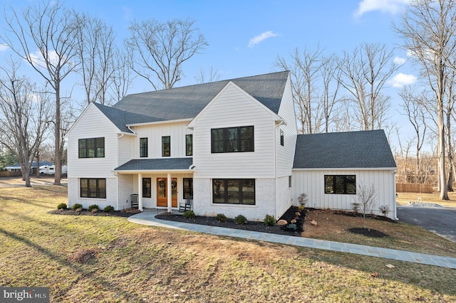 modern inspired farmhouse with brick siding, board and batten siding, a front lawn, and roof with shingles