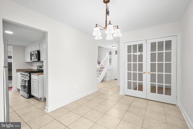 unfurnished dining area featuring light tile patterned floors, baseboards, stairs, and an inviting chandelier