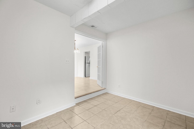 unfurnished room with light tile patterned floors, baseboards, visible vents, and an inviting chandelier