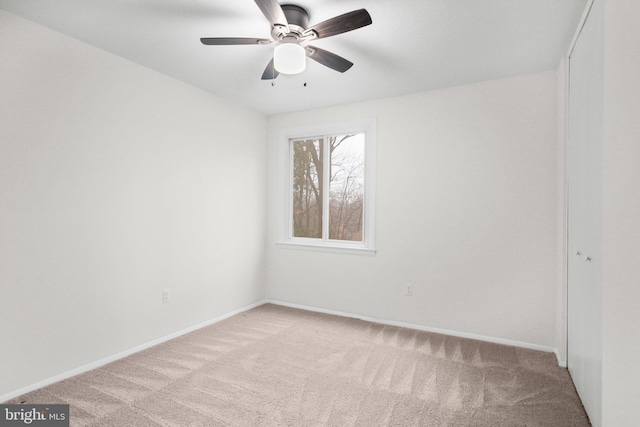 carpeted spare room featuring ceiling fan and baseboards