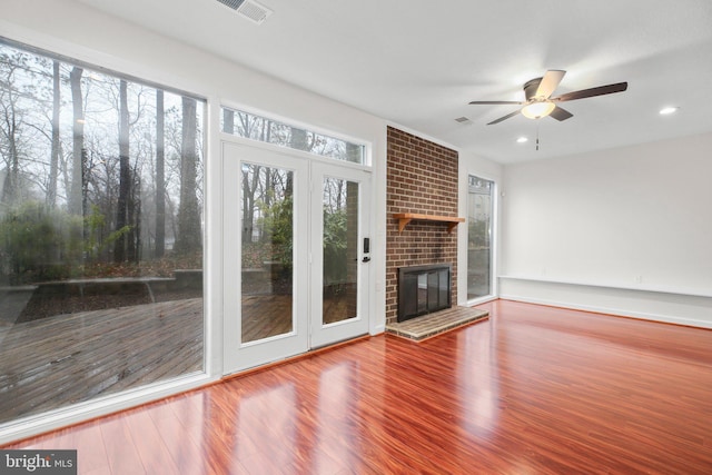 unfurnished living room with ceiling fan, a fireplace, visible vents, and wood finished floors