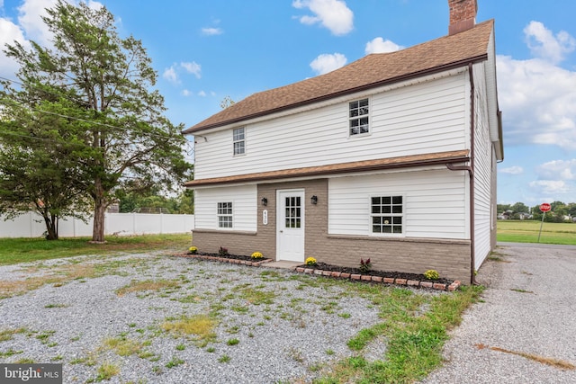 view of front of home with brick siding, a chimney, a shingled roof, and fence