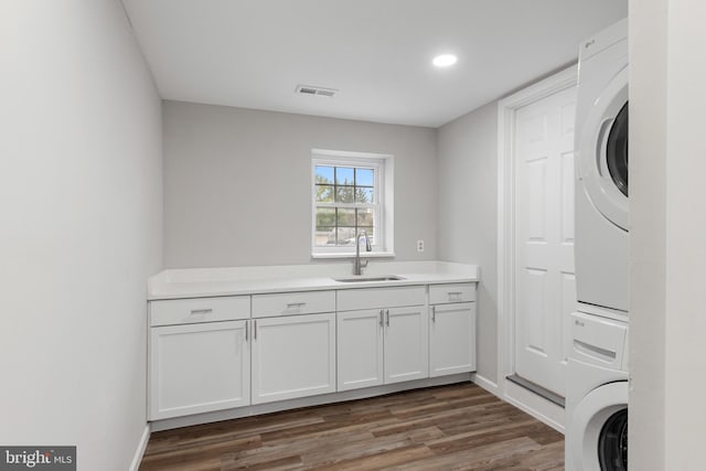 clothes washing area featuring dark wood-style flooring, cabinet space, visible vents, stacked washer / dryer, and a sink