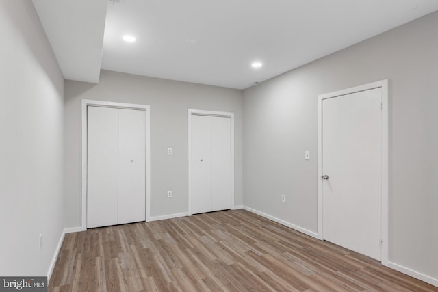 unfurnished bedroom with recessed lighting, baseboards, light wood finished floors, and two closets