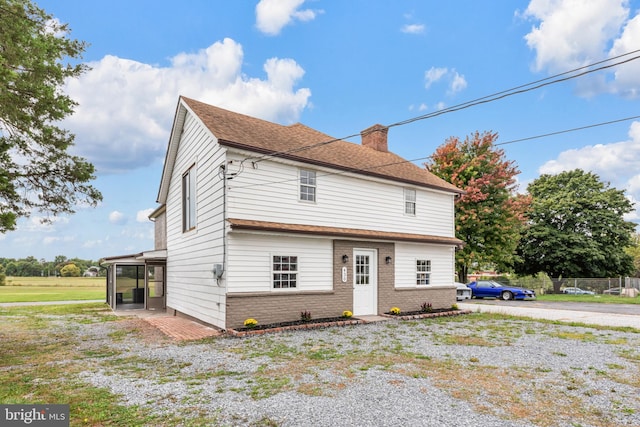 view of front of house with a shingled roof, brick siding, and a chimney