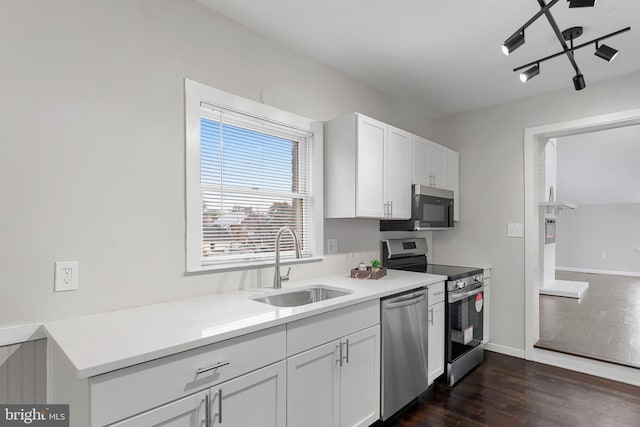 kitchen featuring dark wood finished floors, stainless steel appliances, white cabinets, a sink, and baseboards