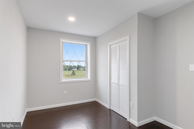 unfurnished bedroom featuring dark wood-type flooring, a closet, and baseboards