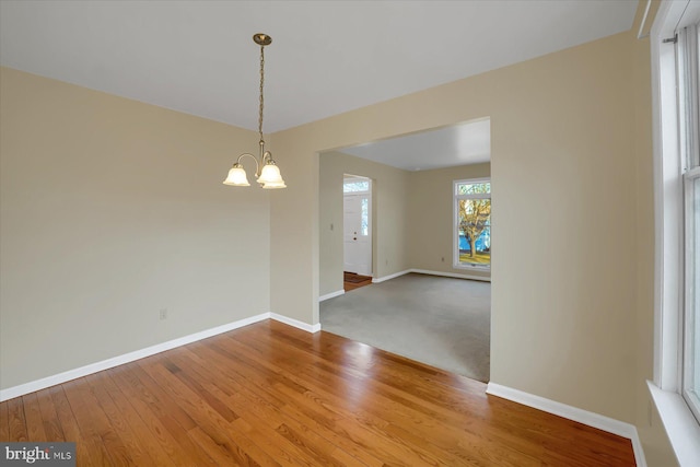 unfurnished room with a chandelier, wood finished floors, and baseboards