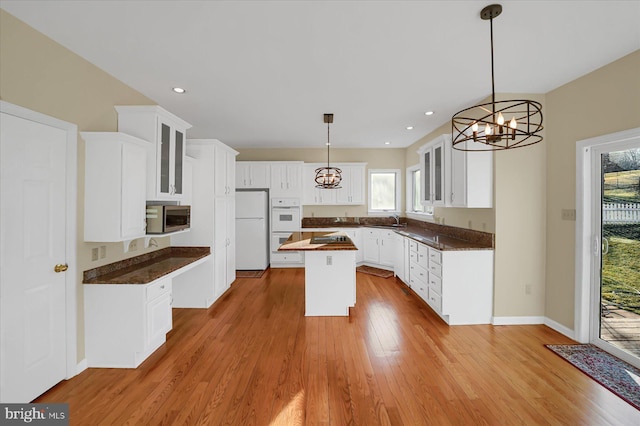 kitchen with a center island, dark countertops, glass insert cabinets, wood finished floors, and white appliances