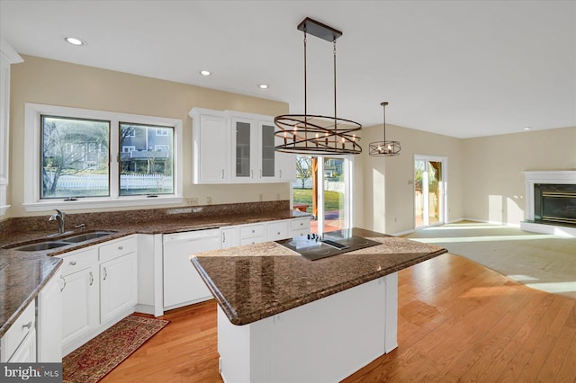 kitchen with black electric cooktop, a sink, open floor plan, dishwasher, and a glass covered fireplace