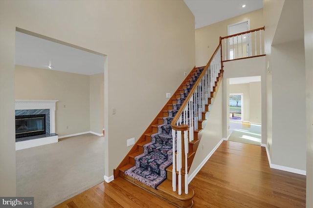 staircase with a towering ceiling, baseboards, wood finished floors, and a high end fireplace