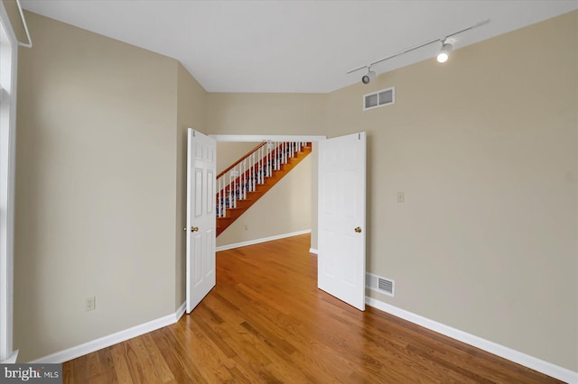 empty room featuring visible vents, stairway, baseboards, and wood finished floors