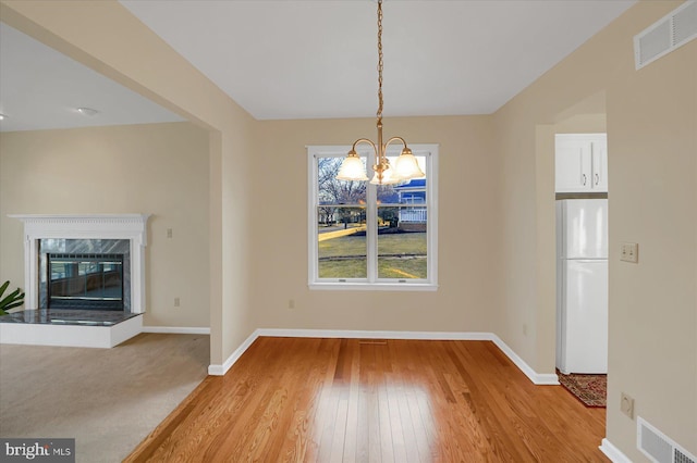 unfurnished dining area with visible vents, a notable chandelier, baseboards, and a premium fireplace