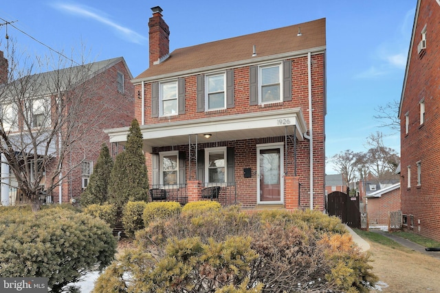 view of front of home featuring a gate, brick siding, a chimney, and covered porch