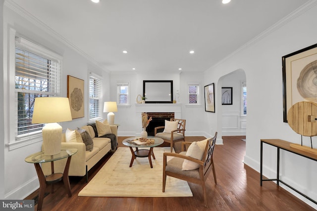 living area with arched walkways, a fireplace, crown molding, and wood finished floors