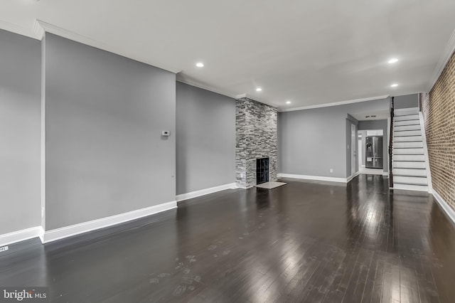 unfurnished living room featuring a stone fireplace, wood finished floors, baseboards, stairs, and crown molding