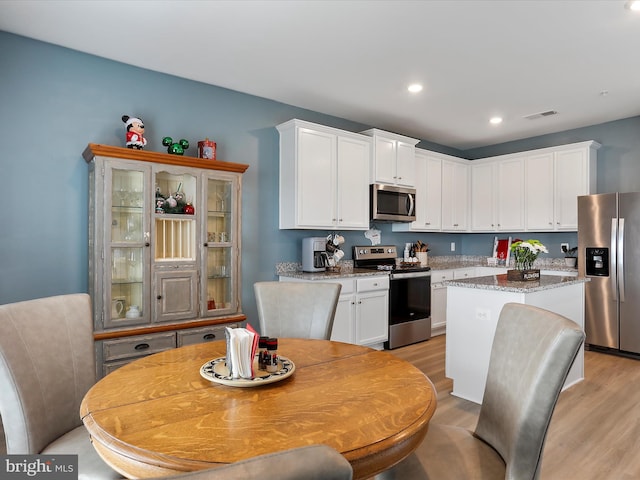 kitchen with stainless steel appliances, light wood finished floors, a kitchen island, and white cabinetry