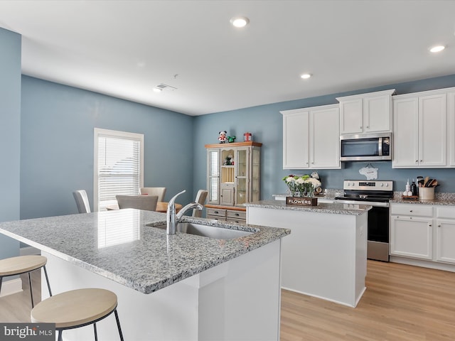 kitchen with a center island with sink, light wood finished floors, a sink, appliances with stainless steel finishes, and white cabinetry