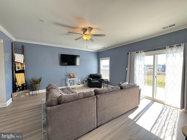 living area with wood finished floors, visible vents, and ornamental molding