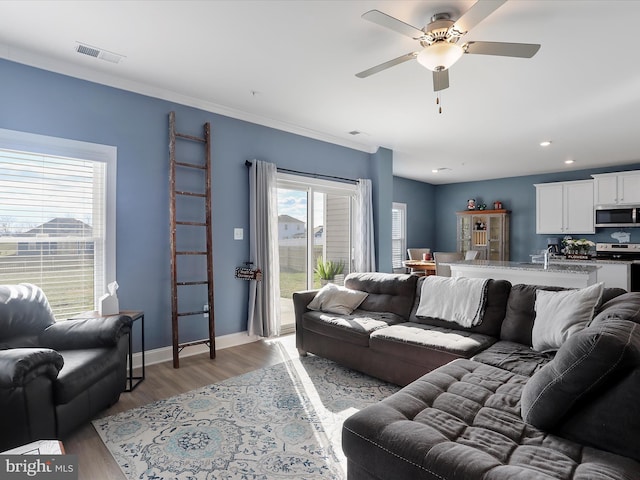 living area featuring light wood-type flooring, baseboards, visible vents, and ornamental molding