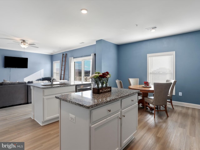 kitchen with a sink, light wood finished floors, stainless steel dishwasher, and a kitchen island