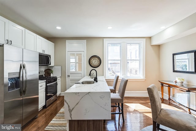 kitchen with appliances with stainless steel finishes, dark wood-type flooring, a sink, and light stone countertops