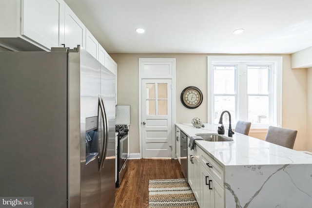 kitchen with stainless steel appliances, a sink, white cabinets, light stone countertops, and dark wood-style floors