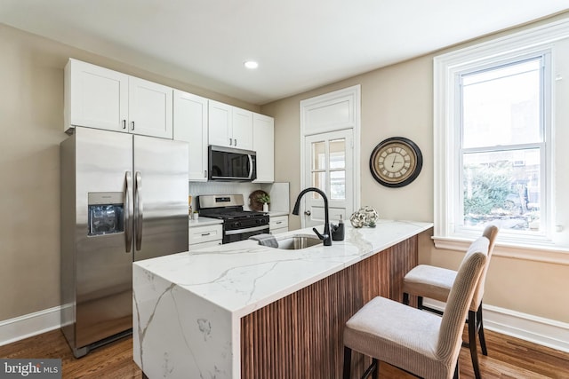 kitchen with light stone counters, a peninsula, wood finished floors, white cabinets, and appliances with stainless steel finishes