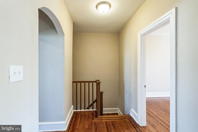 hallway with arched walkways, wood finished floors, an upstairs landing, and baseboards