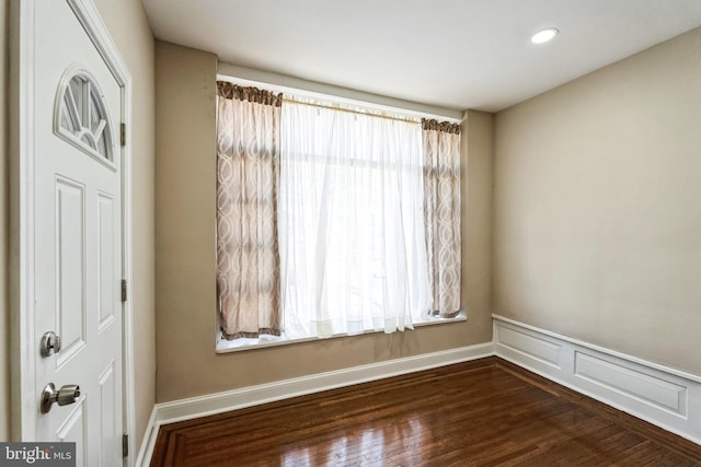 unfurnished room featuring wainscoting, wood finished floors, and a decorative wall