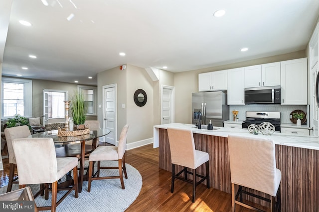 kitchen with recessed lighting, dark wood-style flooring, white cabinetry, appliances with stainless steel finishes, and a kitchen bar