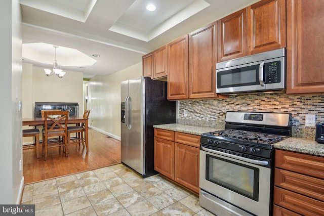 kitchen with decorative backsplash, baseboards, a raised ceiling, a notable chandelier, and stainless steel appliances