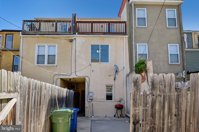 rear view of property featuring stucco siding, a balcony, and fence