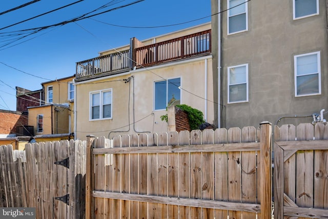 view of property exterior featuring stucco siding, a gate, fence, and a balcony