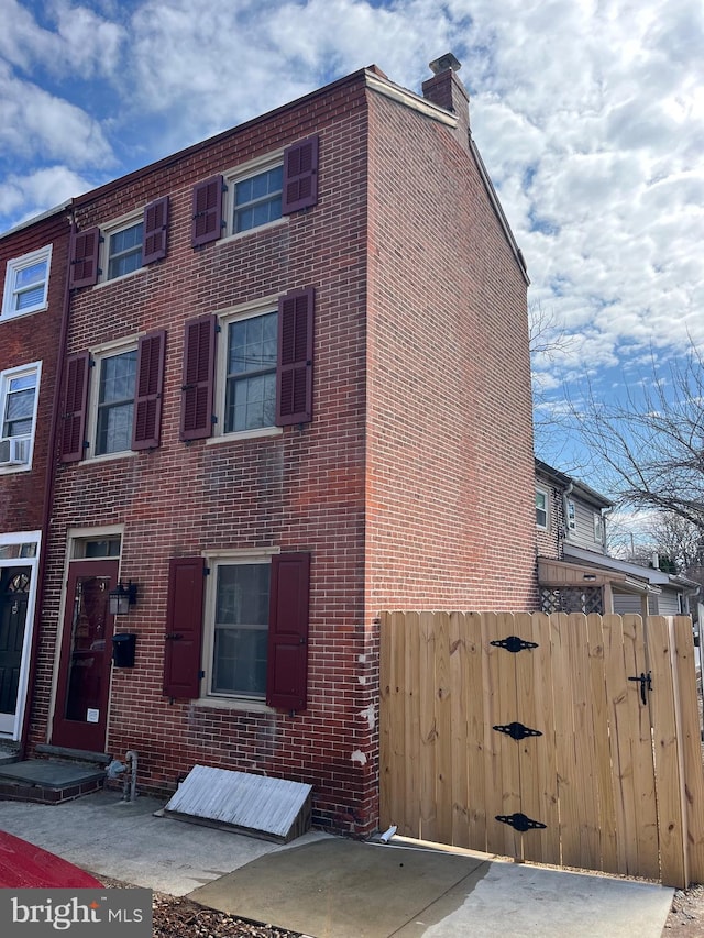 view of front of home with a gate, fence, brick siding, and a chimney