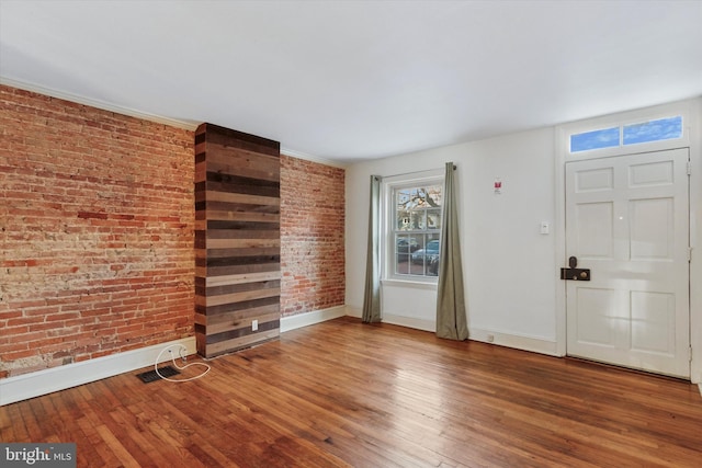 unfurnished living room featuring baseboards, hardwood / wood-style floors, and brick wall