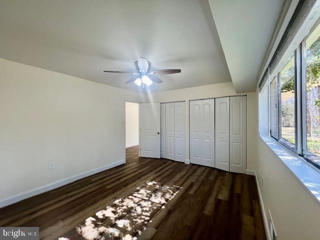 unfurnished bedroom with multiple windows, baseboards, dark wood-style flooring, and multiple closets