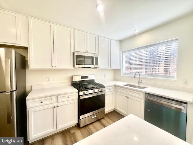 kitchen featuring stainless steel appliances, white cabinets, a sink, and wood finished floors