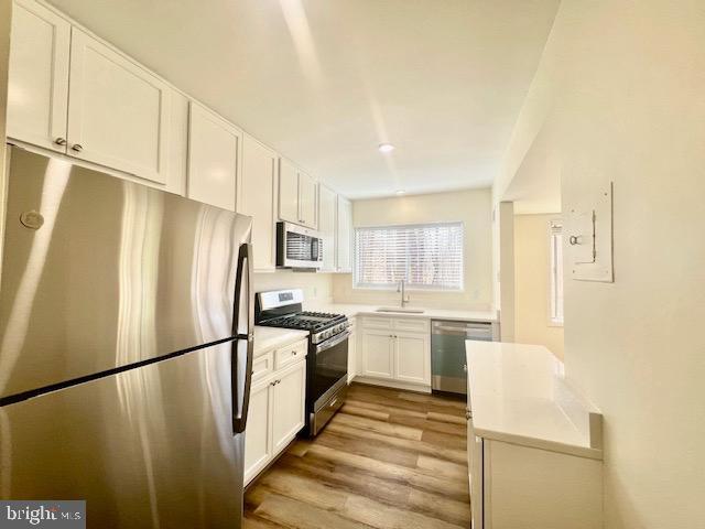 kitchen with stainless steel appliances, light countertops, light wood-type flooring, white cabinetry, and a sink